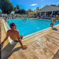Personne au bord de la piscine du camping L'Albizia, avec des visiteurs dans l'eau.
