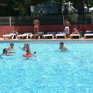 Famille nageant dans la piscine, enfants en anneau flottant, chaises longues à l'arrière-plan - Camping Cap Agathois