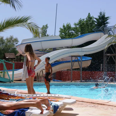 Une piscine avec toboggan à l’eau et des palmiers autour du Camping Cap Agathois.