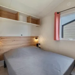 MH Confort + 3CH – 6P - Camping Paradis Les Jonquilles, chambre avec lit, étagères et fenêtre