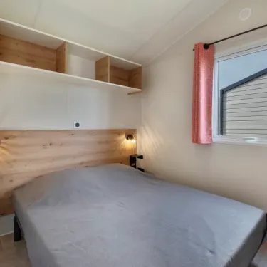 MH Confort + 3CH – 6P - Camping Paradis Les Jonquilles, chambre avec lit, étagères et fenêtre