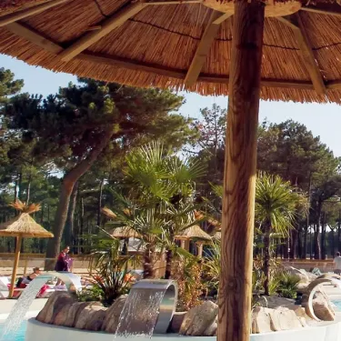 Ombrelle en paille au Camping Atlantique Club Montalivet, avec piscine et arbres en arrière-plan.
