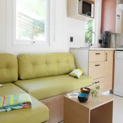 Mobil Home Aqua 3 Chambres 6/8 Personnes Clim TV - Domaine du Golfe de Saint-Tropez : salon avec canapé vert et cuisine intégrée