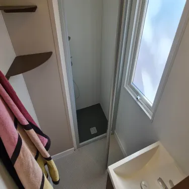 Salle de bain du mobil home avec douche, lavabo et fenêtre
