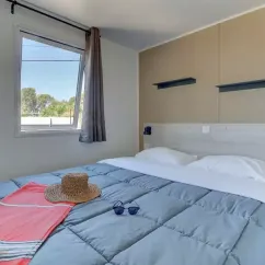 Chambre avec lit double, rideau, et détails de literie dans Mobil Home Aqua 3 Chambres 6 Personnes Clim - Domaine de Kermario