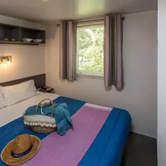Chambre du Mobil Home Aqua, lit double, rideaux, panier, chapeau
