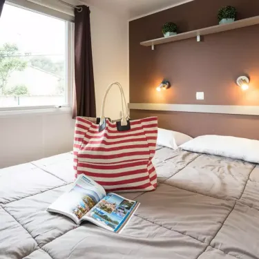 Chambre avec lit, sac à dos et magazine, mobil home Le Soleil des Landes