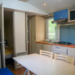 Mobil Home Aqua 2 chambres : cuisine avec table et chaises, vue sur chambre