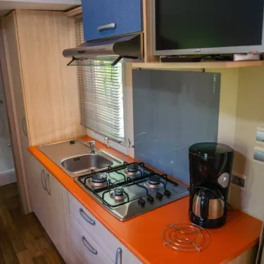 Cuisine du Mobil Home avec plan de travail orange, four, évier et TV