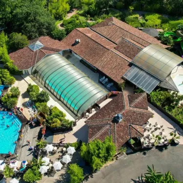 Camping Le Sen-Yan : piscine extérieure avec toboggan vert et structures en toit de tuiles.