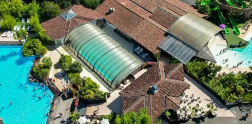 Camping Le Sen-Yan : piscine extérieure avec toboggan vert et structures en toit de tuiles.