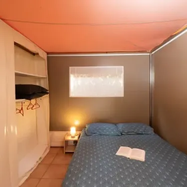 Chambre dans le camping Le Lac des Sapins, lit double, étagères, lampe.