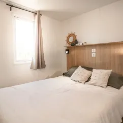 Chambre du Mobil Home Aqua, lit double, tête de lit en bois, fenêtre, rideau