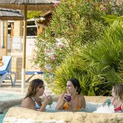 Trois femmes profitent d'un bain chaud avec des boissons colorées au Camping l’Évasion.