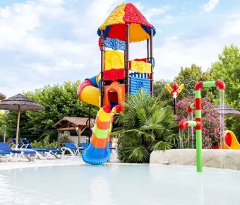 Piscine avec toboggan coloré et parasols en paille au Camping l’Évasion