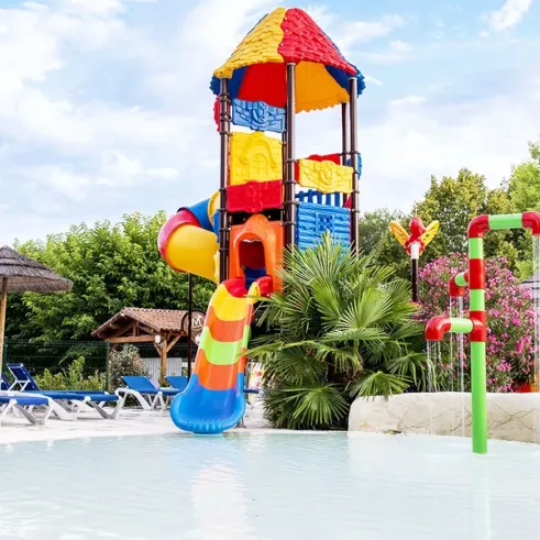 Piscine avec toboggan coloré et parasols en paille au Camping l’Évasion