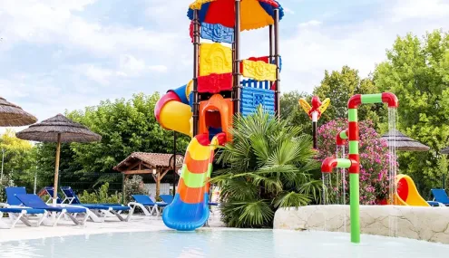 Piscine avec toboggan coloré et parasols en paille au Camping l’Évasion