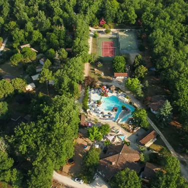 Vue aérienne du camping entouré de forêt, avec piscine, terrain de tennis et installations.