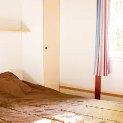 Chambre avec lit simple et rideau coloré dans le chalet Camping l'Évasion