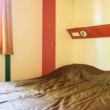 Chambre du chalet Autoire, lit avec drap marron, rideau et armoire.
