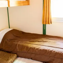 Chambre du chalet Autoire, lit avec drap marron, rideau et fenêtre.