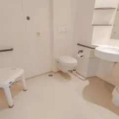 Salle de bain accessible du mobil home Hélios, avec toilettes, lavabo et chaise roulante.