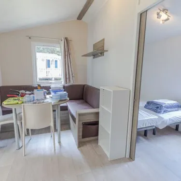 Salle à manger et coin lit du mobil home Hélios, avec canapé, table et lit pliant.