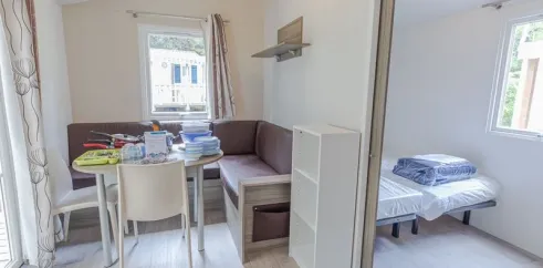 Salle à manger et coin lit du mobil home Hélios, avec canapé, table et lit pliant.