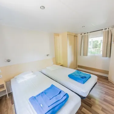 Mobil Home Hélios 2 Chambres 4 Personnes PMR - La Ferme, chambre avec 2 lits et rideaux