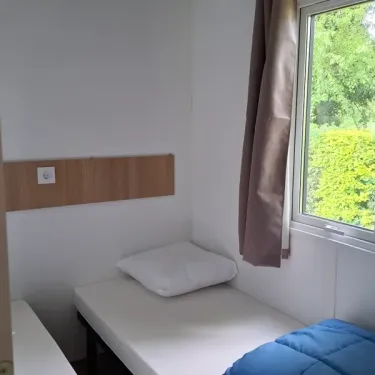 Chambre du mobil home L'Orchis des Marais avec lit, rideau, et fenêtre