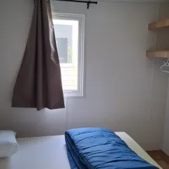 Chambre du mobil home L'Orchis des Marais avec lit, rideau, et étagères