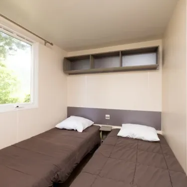 Mobil Home Confort 3 Chambres 6 personnes - Camping Paradis L'Europe : chambre avec deux lits simples et étagères murales