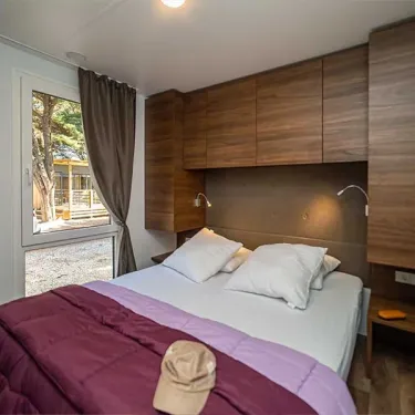 Chambre dans le Mobil Home Hélios, lit double, rangements en bois, vue sur le jardin.