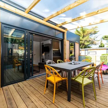 Terrasse extérieure du Mobil Home Hélios avec table, chaises colorées et toit en bois.