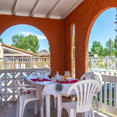 Terrasse du bungalow Alizé, table et chaises blanches, vue sur le camping