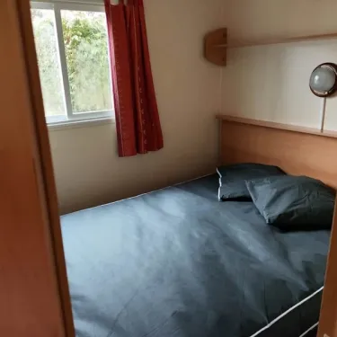 Mobil Home Jacinthe - Chambre avec lit, rideau rouge et miroir mural