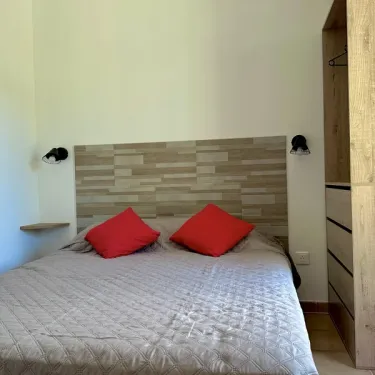 Chambre avec lit double, tête de lit en bois et deux oreillers rouges - Cottage Premium - Camping Village de Vacances Camboussel