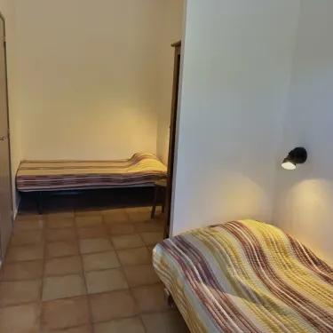 Chambre avec deux lits simples et lampe murale au Camping Village de Vacances Camboussel