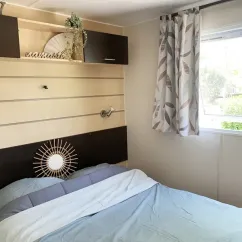 Mobil Home Welcome 3CH 6P - Camping Val de Cesse : chambre avec lit, miroir et étagères