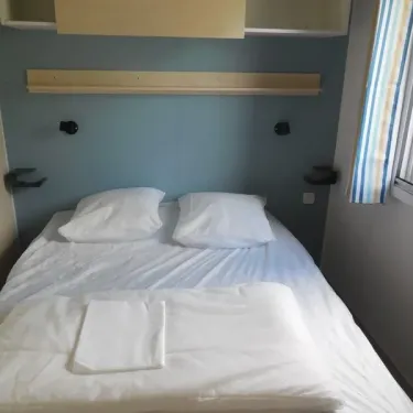 Mobil Home 2 Personnes - Camping du Lac Terre d'Auge : lit double avec draps blancs et étagères murales