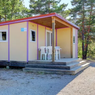 Bungalow Le Lavandin avec terrasse et chaises blanches, entouré de pins.