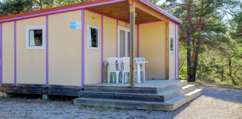 Bungalow Le Lavandin avec terrasse et chaises blanches, entouré de pins.