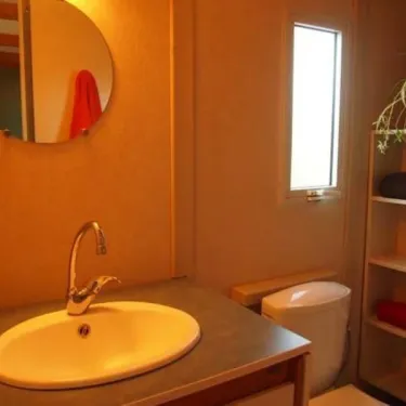 Salle de bain du bungalow Le Lavandin avec lavabo, toilettes et miroir rond.
