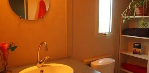 Salle de bain du bungalow Le Lavandin avec lavabo, toilettes et miroir rond.