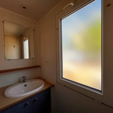 Salle de bain avec lavabo, miroir et fenêtre fumée - Mobil Home Eco 2 Chambres 4 Personnes Clim TV - Paradis Family les Rives de l'Hérault