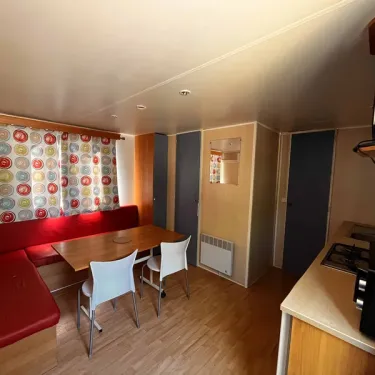 Coin repas avec canapé rouge, table, chaises et cuisine - Mobil Home Eco 2 Chambres 4 Personnes Clim TV - Paradis Family les Rives de l'Hérault