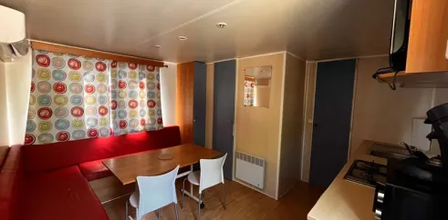 Coin repas avec canapé rouge, table, chaises et cuisine - Mobil Home Eco 2 Chambres 4 Personnes Clim TV - Paradis Family les Rives de l'Hérault