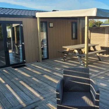 Terrasse en bois avec canapé et table de pique-nique devant mobil home