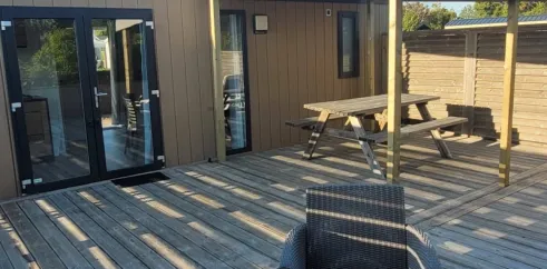 Terrasse en bois avec canapé et table de pique-nique devant mobil home