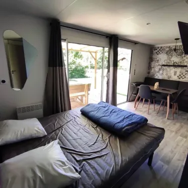 Chambre du mobil home avec lit, rideaux et accès à la terrasse - Family's Camping Le Savoy